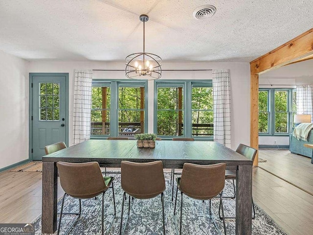 dining space featuring light wood-type flooring, a notable chandelier, visible vents, and a textured ceiling