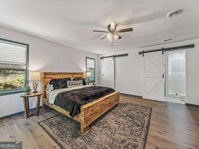 bedroom featuring baseboards, a barn door, visible vents, and wood finished floors