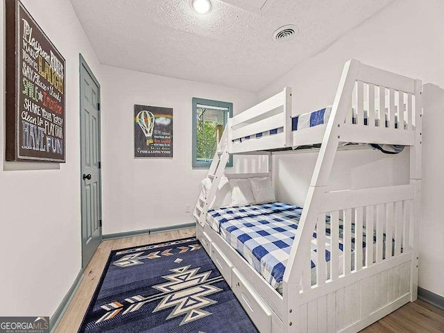 bedroom with baseboards, a textured ceiling, visible vents, and wood finished floors