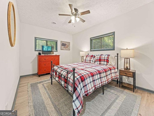 bedroom with a textured ceiling, wood finished floors, visible vents, and baseboards