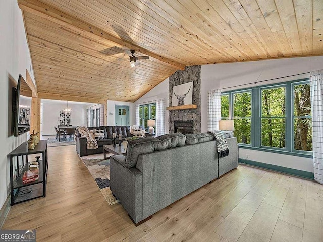 living room featuring vaulted ceiling with beams, a healthy amount of sunlight, light wood-style flooring, and a stone fireplace