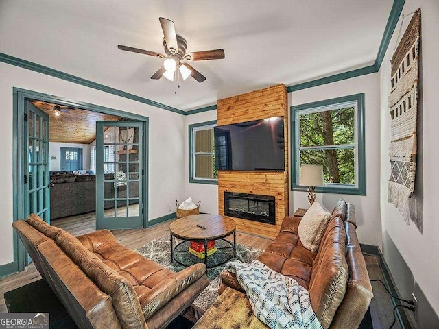 living area featuring ornamental molding, a large fireplace, ceiling fan, wood finished floors, and baseboards