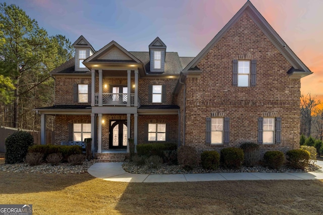 view of front facade with brick siding, covered porch, a lawn, and a balcony