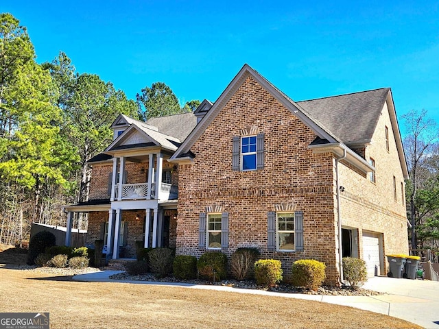 traditional-style home featuring brick siding, a shingled roof, concrete driveway, a garage, and a balcony