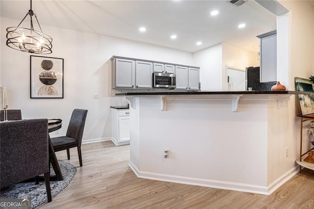 kitchen with dark countertops, stainless steel microwave, gray cabinetry, and a breakfast bar area