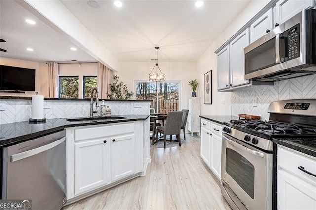 kitchen featuring appliances with stainless steel finishes, dark stone countertops, a sink, and pendant lighting