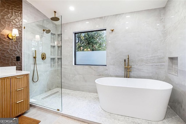 full bath featuring a freestanding bath, tile walls, vanity, and a walk in shower