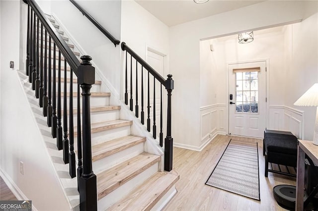 foyer featuring a wainscoted wall, stairway, light wood-type flooring, and a decorative wall