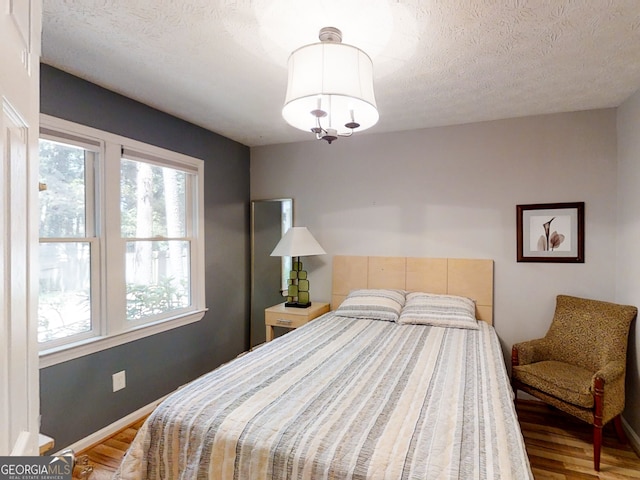 bedroom with a textured ceiling, wood finished floors, and baseboards