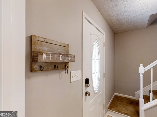 foyer entrance with stairs, baseboards, and a textured ceiling