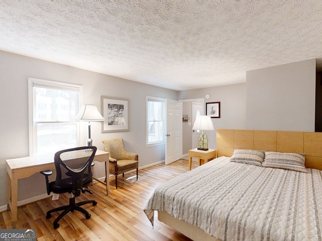 bedroom with baseboards, multiple windows, a textured ceiling, and light wood finished floors