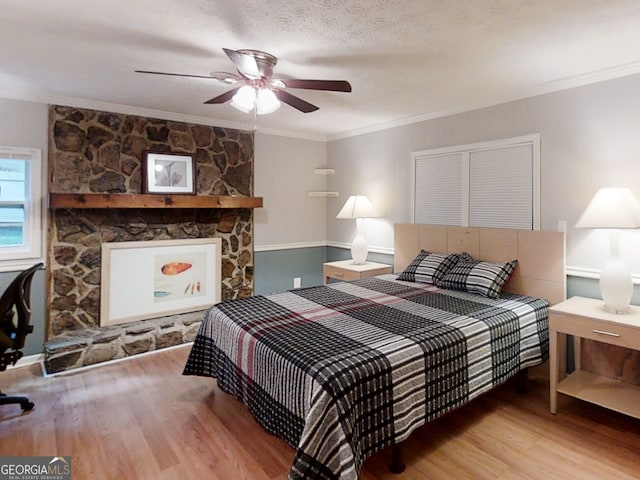 bedroom featuring a fireplace, crown molding, a textured ceiling, and light wood finished floors