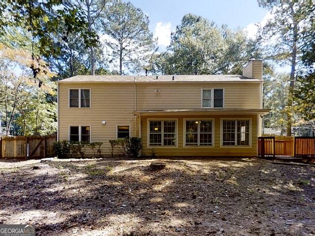 rear view of house featuring a chimney and fence