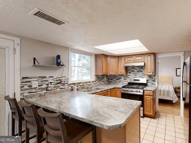 kitchen with visible vents, gas range, a breakfast bar area, under cabinet range hood, and light tile patterned flooring