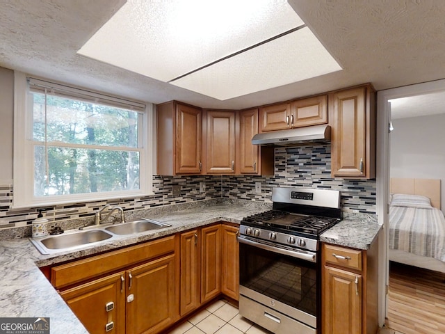 kitchen featuring light countertops, backsplash, stainless steel range with gas stovetop, a sink, and under cabinet range hood