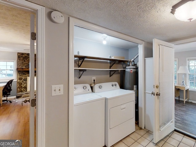 washroom featuring a textured ceiling, light tile patterned floors, laundry area, water heater, and washing machine and clothes dryer