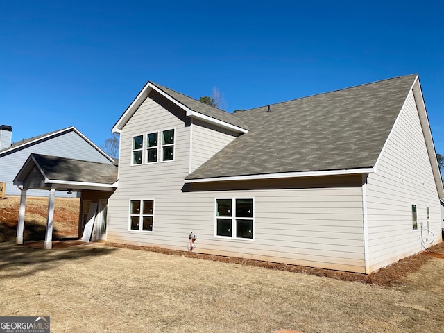 rear view of house with a lawn and roof with shingles