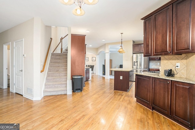 kitchen with hanging light fixtures, light wood-style floors, stainless steel fridge, and a kitchen island