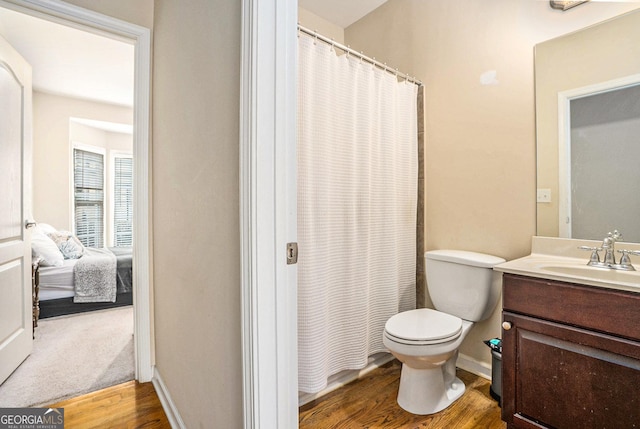 ensuite bathroom featuring connected bathroom, toilet, wood finished floors, vanity, and baseboards