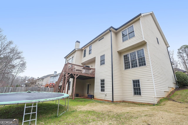 back of house featuring a deck, stairway, a lawn, a trampoline, and a chimney