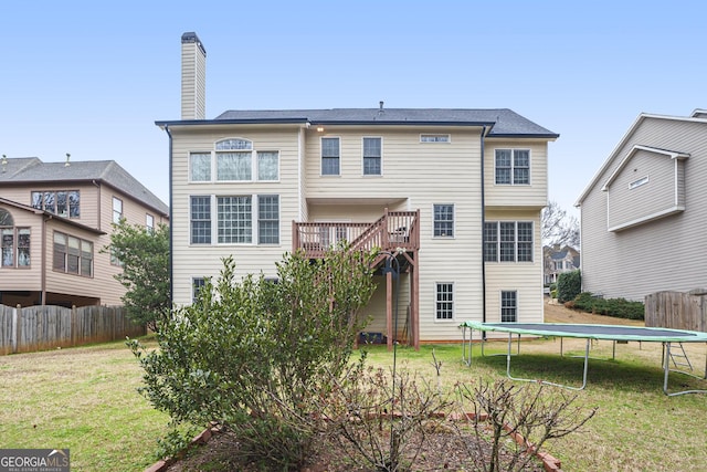 back of house with a trampoline, a yard, fence, and a chimney