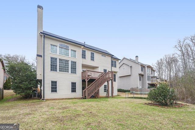 back of property with a lawn, a chimney, stairway, a trampoline, and a wooden deck