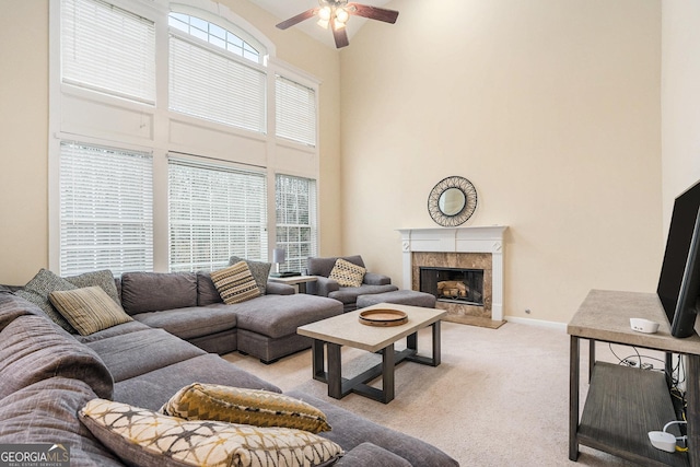 living room with a towering ceiling, a premium fireplace, a ceiling fan, light carpet, and baseboards