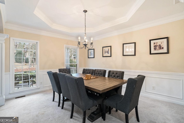 dining area featuring a wainscoted wall, a notable chandelier, a raised ceiling, light colored carpet, and visible vents