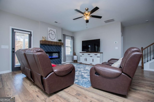 living area with wood finished floors, a ceiling fan, a tile fireplace, and stairway