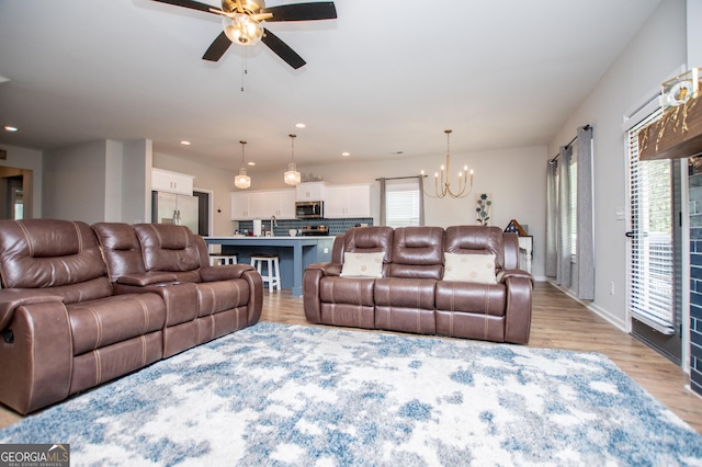living room with a chandelier, light wood-type flooring, ceiling fan, recessed lighting, and baseboards