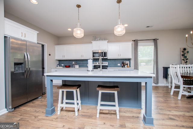 kitchen featuring stainless steel appliances, backsplash, light countertops, white cabinetry, and a center island with sink