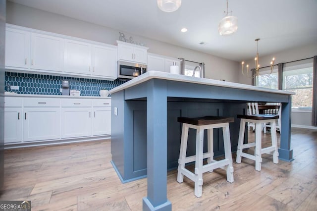 kitchen with stainless steel microwave, a chandelier, white cabinetry, a breakfast bar area, and hanging light fixtures