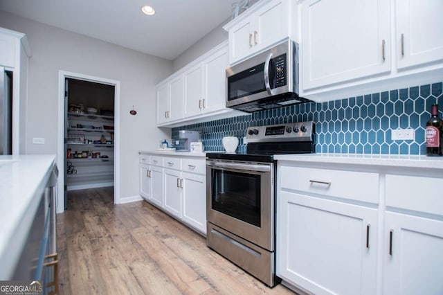 kitchen featuring stainless steel appliances, light countertops, decorative backsplash, white cabinetry, and light wood-style floors