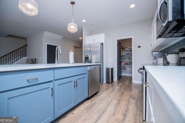 kitchen featuring appliances with stainless steel finishes, a sink, light countertops, hanging light fixtures, and light wood finished floors
