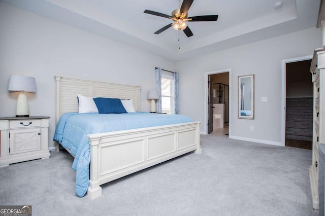 bedroom with light carpet, a raised ceiling, baseboards, a ceiling fan, and ensuite bathroom