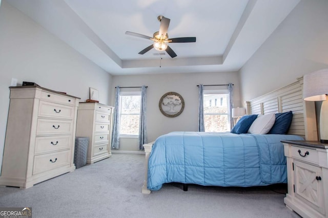 bedroom featuring a tray ceiling, light colored carpet, baseboards, and ceiling fan