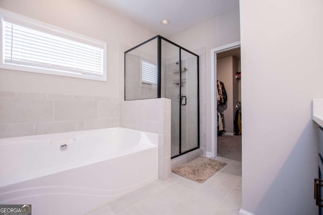 bathroom with tile patterned flooring, a garden tub, a stall shower, a spacious closet, and baseboards
