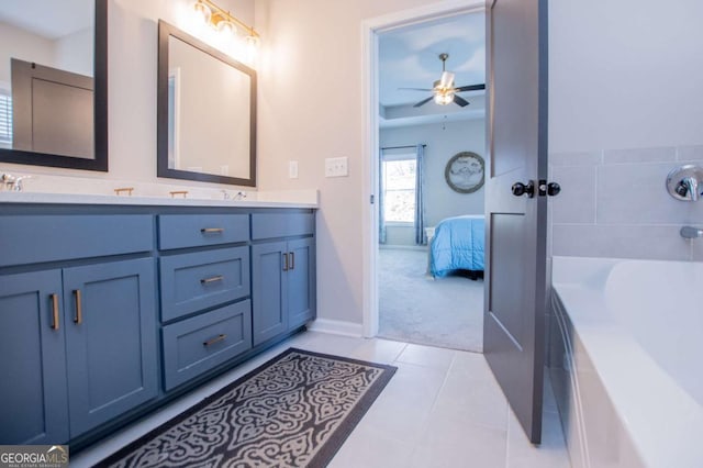 ensuite bathroom featuring a ceiling fan, a bath, double vanity, and baseboards