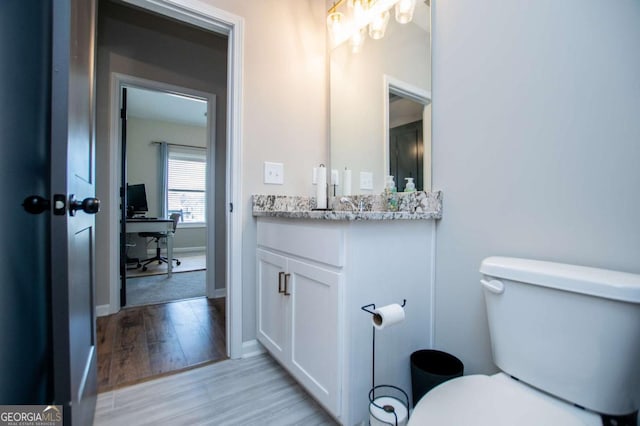 bathroom with toilet, vanity, baseboards, and wood finished floors