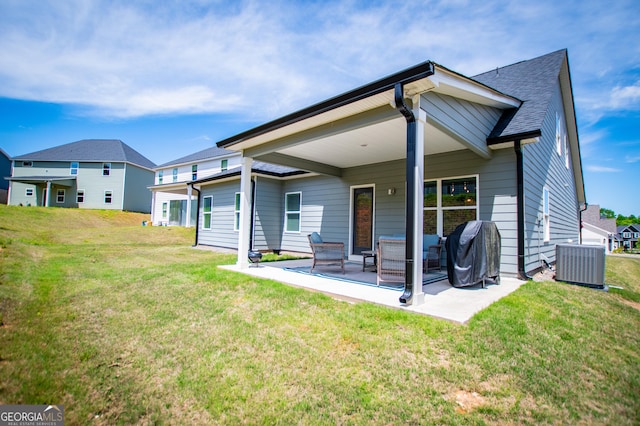 rear view of property with cooling unit, a patio, a yard, and a shingled roof
