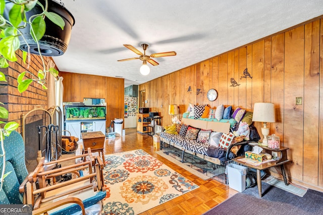 living room with wood walls, ceiling fan, a brick fireplace, and a textured ceiling