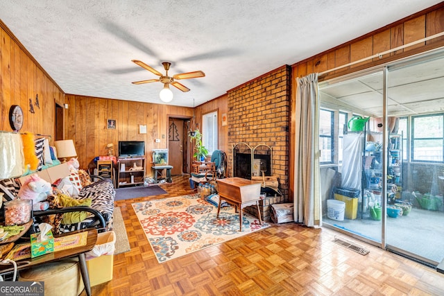 living area featuring a brick fireplace, visible vents, wood walls, and a textured ceiling