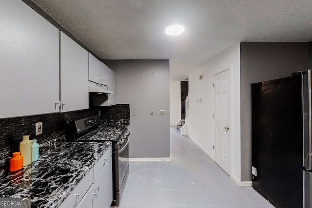 kitchen featuring under cabinet range hood, white cabinetry, stainless steel range with gas cooktop, freestanding refrigerator, and tasteful backsplash