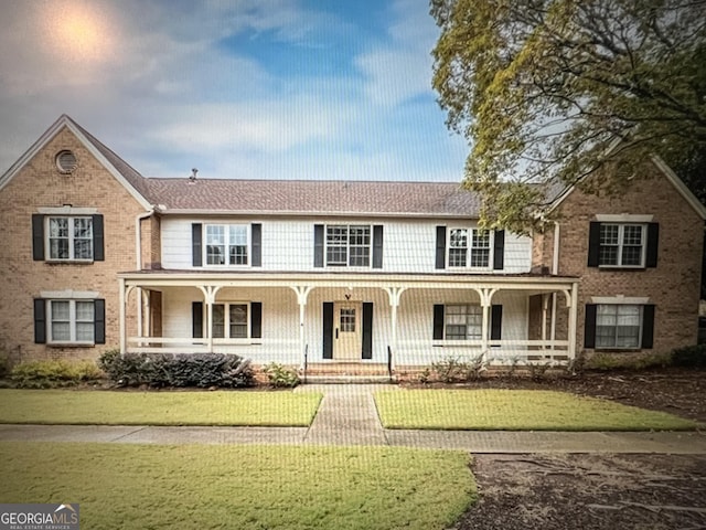 view of front of house featuring covered porch, brick siding, and a front yard