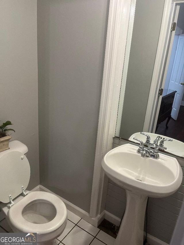 half bath featuring baseboards, a sink, toilet, and tile patterned floors