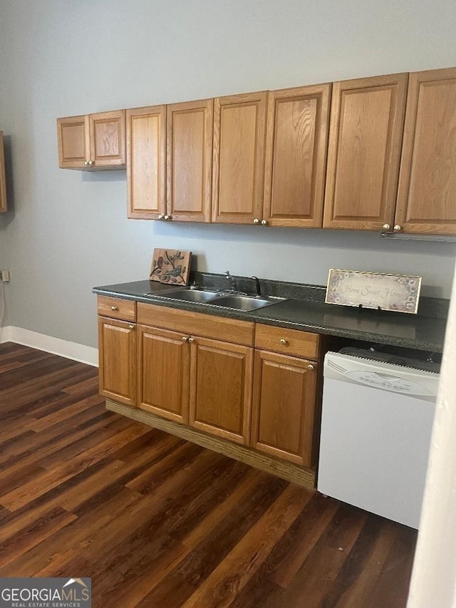 kitchen with dark countertops, dark wood-style flooring, white dishwasher, and a sink