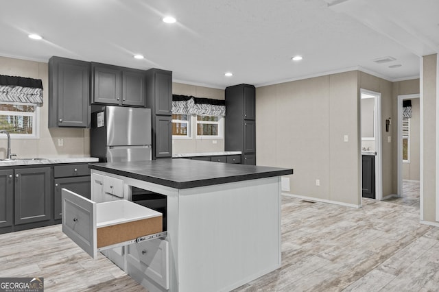 kitchen with a center island, freestanding refrigerator, crown molding, gray cabinetry, and a sink