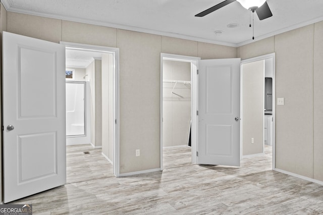 unfurnished bedroom with light wood-type flooring, a closet, a walk in closet, and crown molding