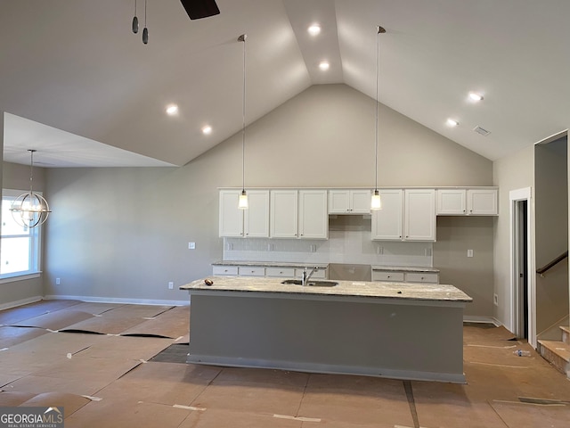 kitchen with light stone counters, a kitchen island with sink, a sink, white cabinetry, and high vaulted ceiling