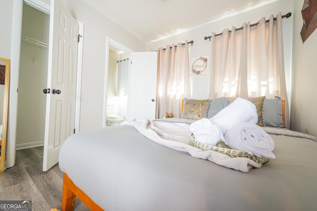 bedroom with ensuite bathroom, multiple windows, a closet, and wood finished floors